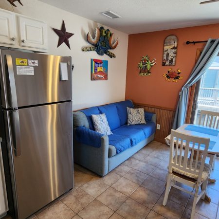 Small kitchen area with a stainless fridge, blue sofa, dining table, and beach-themed wall decorations.