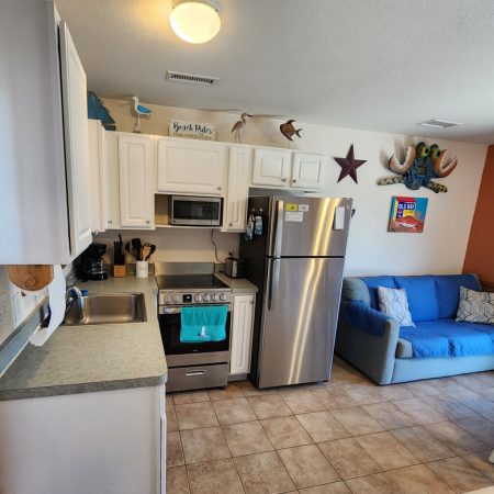 Small kitchen with white cabinets, stainless steel appliances, and a blue couch in an open living space with tile floor.
