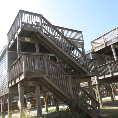 Elevated beach house with multiple wooden staircases and decks under a clear blue sky.