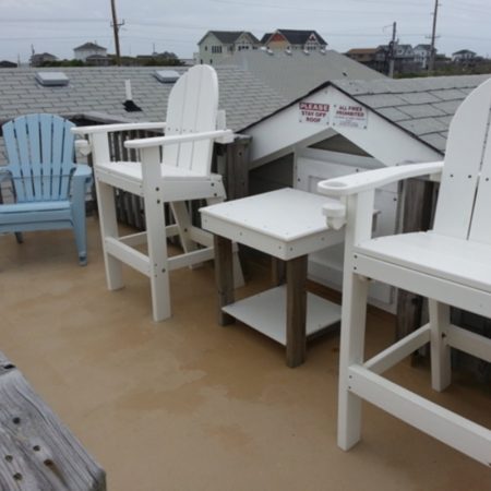 Two tall white chairs, a blue chair, and a small table are arranged on a rooftop deck with a view of houses.