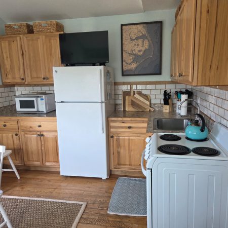Small kitchen with wood cabinets, white appliances, a blue kettle on the stove, and a map on the wall above the sink.