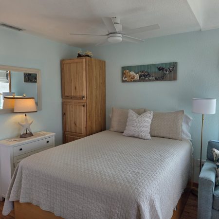 Bedroom with a neatly made bed, wooden wardrobe, lamp on side table, wall art, and a window with natural light.