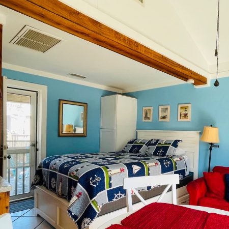 Bedroom with nautical decor, blue walls, a white bed, red sofa, wardrobe, and a door leading to a balcony.