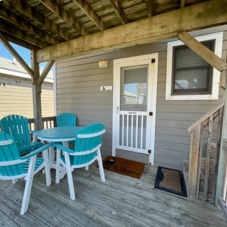 Small porch with turquoise chairs and table, wooden floor, and a white screen door with welcome mats.
