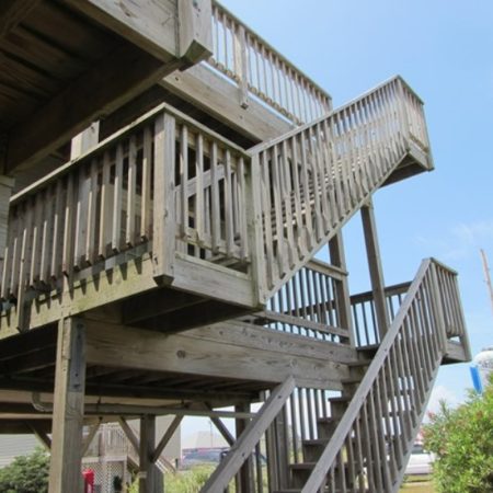 Wooden outdoor staircase with railings, viewed from below, leading up to multiple levels under a clear sky.