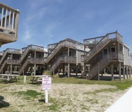 Elevated beach houses with wooden stairs and a sign reading “Private Property, No Trespassing” in the foreground.