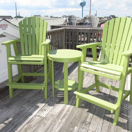 Two green Adirondack chairs and a small round table on a weathered wooden deck in daylight.