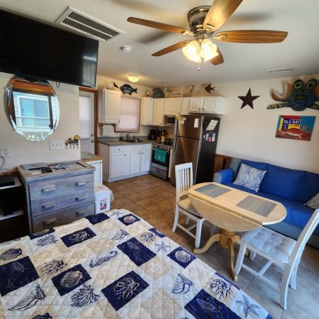 Small kitchen and dining area with a bed, sofa, and wall decor in a compact studio apartment.