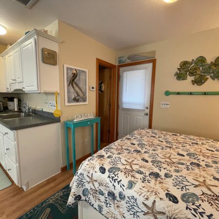 Small kitchen and bedroom space with coastal decor, a turquoise table, and a bed with a seashell-patterned comforter.