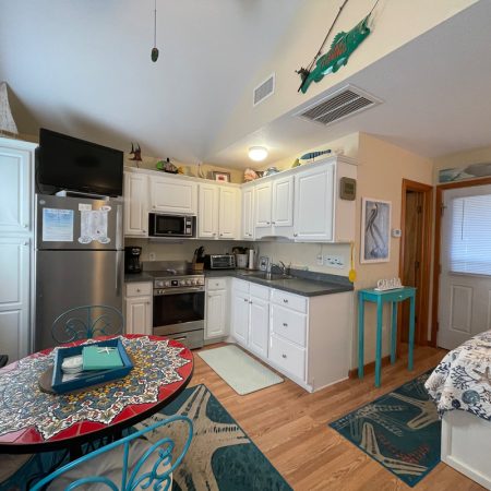 Small kitchen with white cabinets, stainless steel appliances, and a round table next to a bed in a cozy studio space.