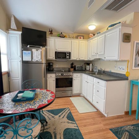 Small kitchen with white cabinets, stainless appliances, round dining table, and blue accents in a cozy space.