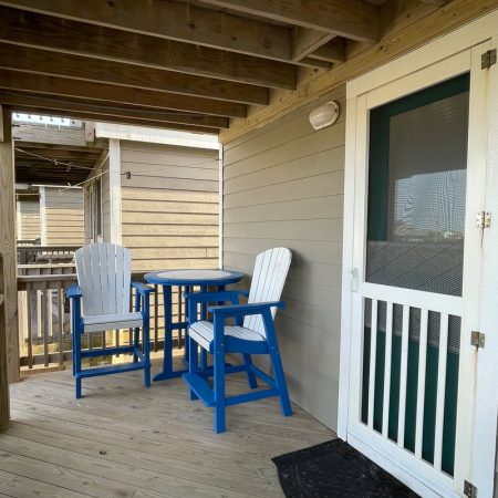 Small porch with two blue and white chairs, a round table, wooden railings, and a screened door to the house.