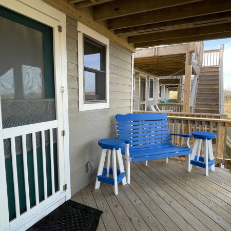 Wooden porch with a blue bench, two blue stools, and a screened door attached to a beige house.