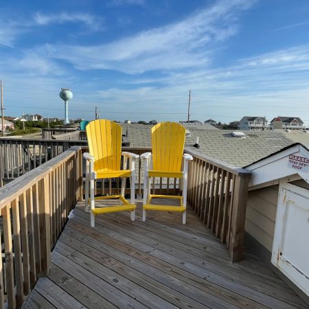 Two yellow chairs on a wooden deck overlook rooftops and a water tower under a blue sky with scattered clouds.