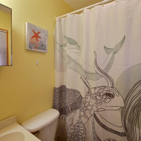 Small bathroom with yellow walls, a sea-themed shower curtain, wall art, and a mirror above the sink.