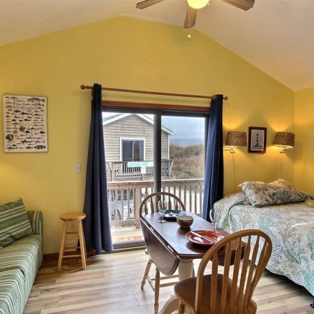 Room with yellow walls, bed, striped sofa, small dining table, and sliding glass door leading to a balcony.