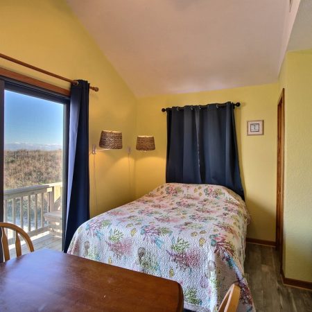 Small bedroom with a single bed, TV, table, and sliding glass door leading to a balcony with an outdoor view.