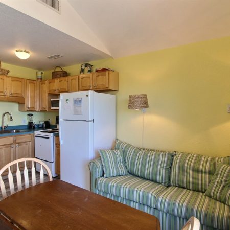 Small kitchen with wood cabinets, white appliances, a striped green sofa, and a wooden dining table with chairs.