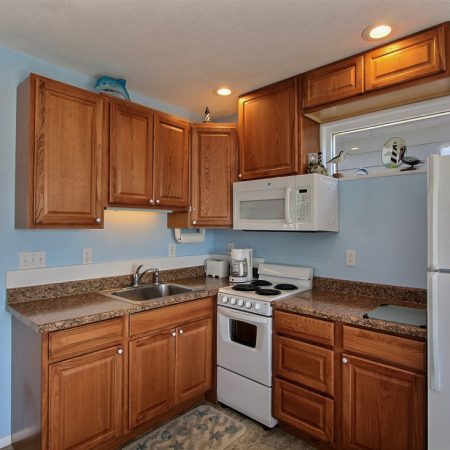 Kitchen with wooden cabinets, granite countertops, sink, dishwasher, stove, and microwave under a window with blinds.