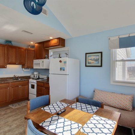 Small kitchen and dining area with wooden cabinets, table, blue accents, and a window letting in natural light.
