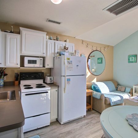 Small kitchen and living area with white appliances, a round mirror, and a window allowing natural light.