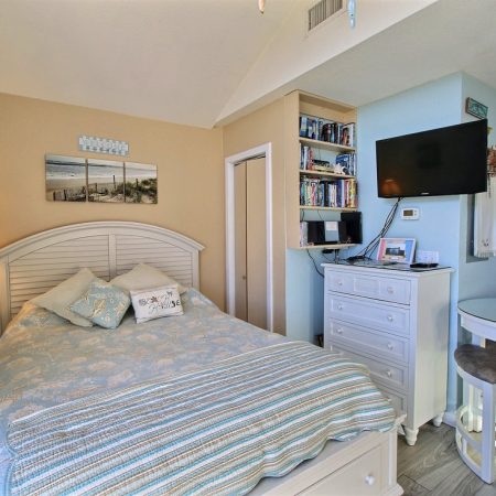 Small bedroom with a bed, TV, dresser, bookshelf, round table with chairs, and coastal-themed decor.