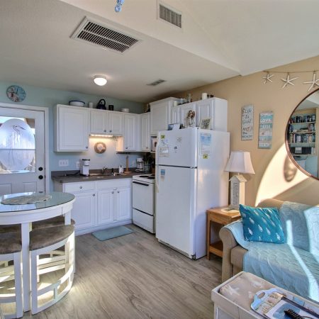 Small coastal-themed kitchen and living area with white cabinets, round table, and beach decor on walls and shelves.