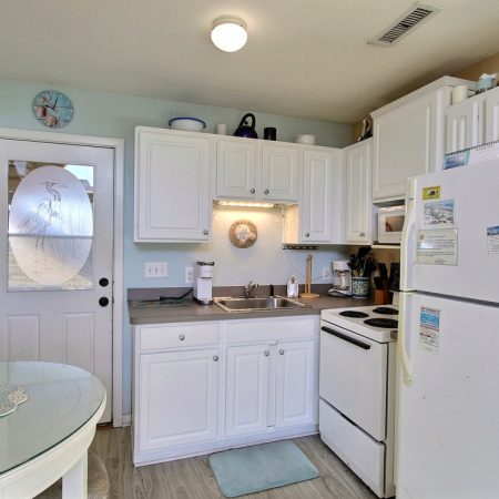 This kitchen has white cabinets, a white stove, fridge, and sink, light blue walls, wood floor, and a round dining table.