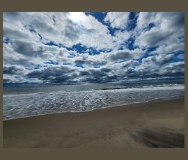 Cloudy sky over a sandy beach with gentle waves approaching the shore under bright daylight.
