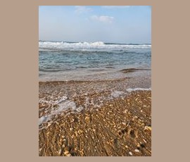 Waves approach a sandy beach covered with small seashells under a partly cloudy sky.