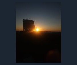 Silhouette of a stilt house at sunset with the sun low on the horizon and a clear sky in the background.