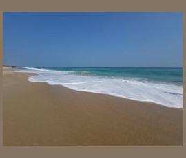 Clear blue sky over a sandy beach with gentle ocean waves coming ashore.