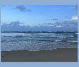 Waves roll onto a sandy beach under a blue sky with scattered clouds at dusk.