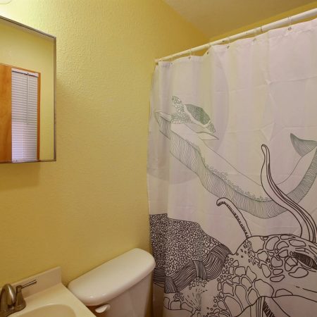 Small bathroom with a yellow wall, mirror, sink, toilet, and a shower curtain with whale illustrations.