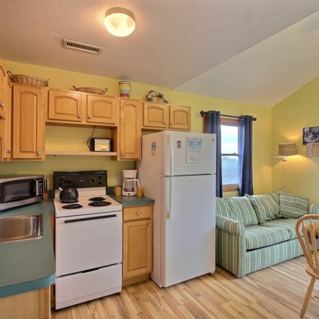 Small kitchen with light wood cabinets, white appliances, and a living area with a striped sofa and dining table.