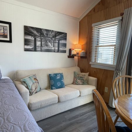 Small living area with a white couch, decorative pillows, wall art, a table, and window with blinds.