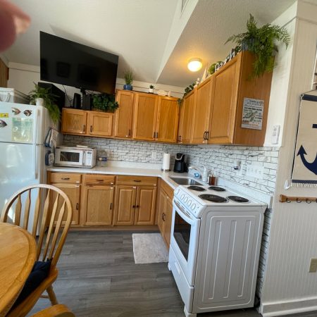 Small kitchen with wooden cabinets, white appliances, round table, and nautical-themed wall decor featuring a blue anchor.