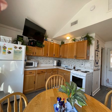 Kitchen with wooden cabinets, white appliances, and a round table with plants in the center of the room.