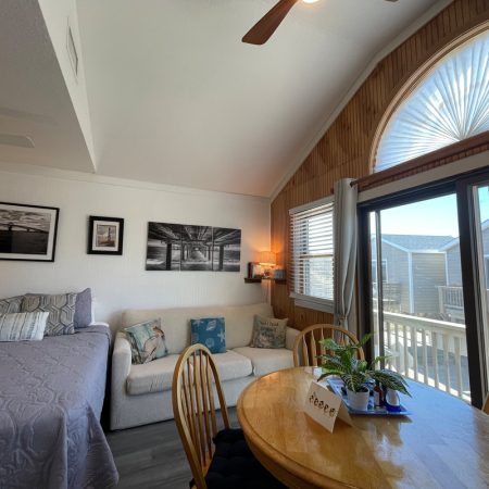 A cozy room with a bed, sofa, dining table, large arched window, and sliding doors opening to a deck.