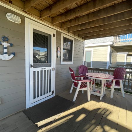 Small porch with a round table, four red chairs, and a white door; anchor decoration on gray wall.