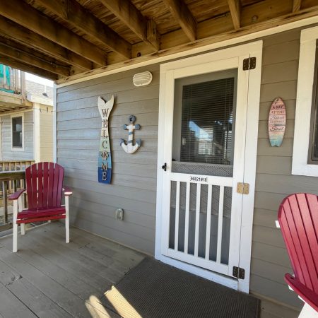 A porch with two red chairs, a white screen door, and nautical-themed decorations on a gray wood-paneled wall.