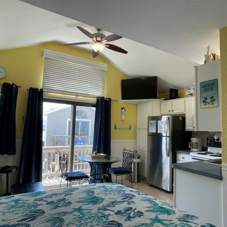 Small, bright studio with a bed, kitchenette, dining table, and sliding doors leading to a sunlit porch.