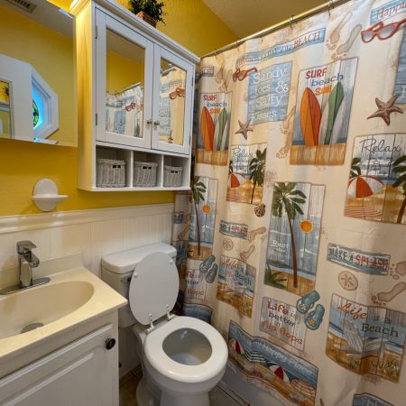 Small bathroom with surf-themed shower curtain, white sink and toilet, wall mirror, and yellow painted walls.