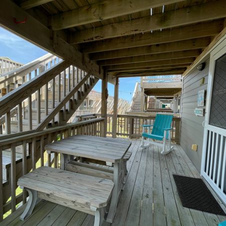 Wooden porch with picnic table, two blue rocking chairs, and stairs leading to upper decks on a sunny day.