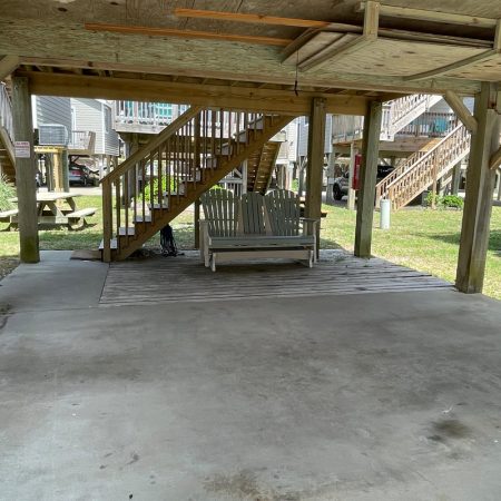 Wooden stairs and a porch swing under a raised house, with picnic tables and grass visible in the background.
