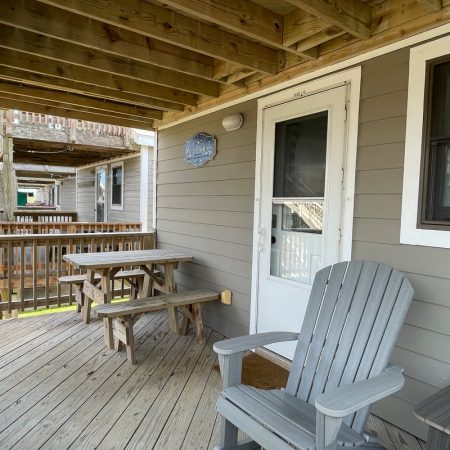 Wooden deck with a picnic table, Adirondack chair, and a door leading into a gray house with white trim.