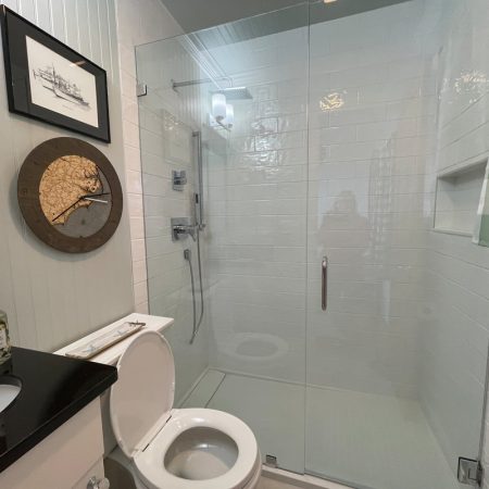 Small bathroom with a glass shower, toilet, sink, wall art, and green plaid curtain.