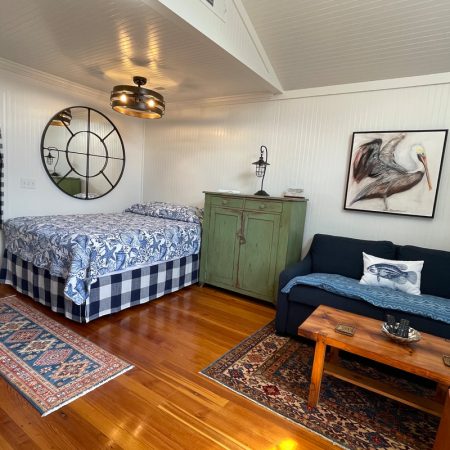 Cozy room with a bed, blue sofa, green cabinet, wall art, wood floors, and decorative rugs.