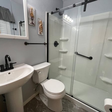 Small bathroom with a pedestal sink, toilet, wall mirror, and a glass-enclosed shower with black fixtures.