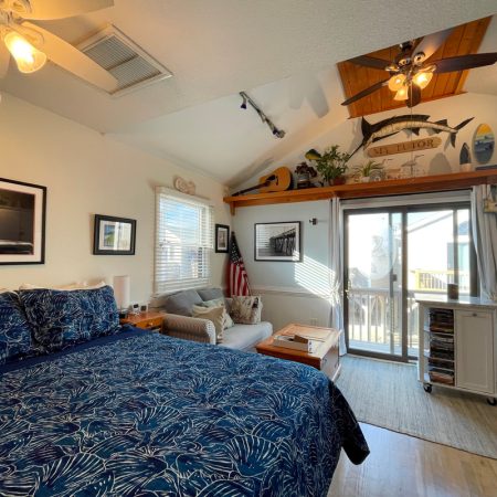 Bedroom with blue-patterned bedding, sofa, wall art, ceiling fans, and sliding glass doors leading to a balcony.